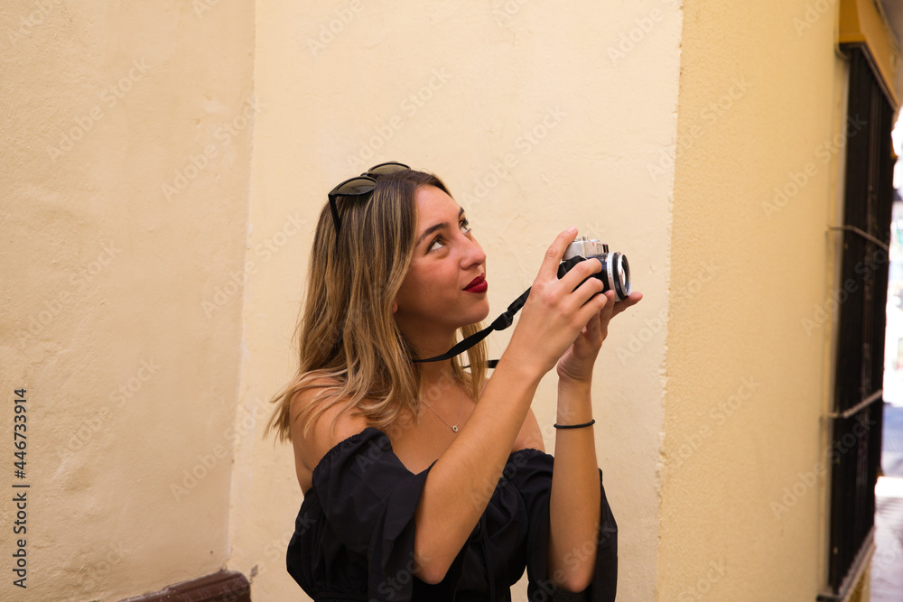 Fototapeta premium Beautiful young woman on holiday. She is taking a photo of a monument in the street. The woman is happy about the city she is visiting. Holiday concept, traveling.