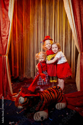 Small girls during a stylized theatrical circus photo shoot in a beautiful red location. Young models posing on stage with curtain. Sisters or female friends together