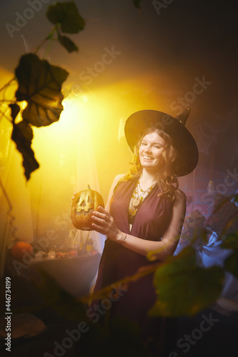 Young slim woman looking like witch having fun on Halloween in a dark room with yellow light and smoke. Carnival concept and Halloween party