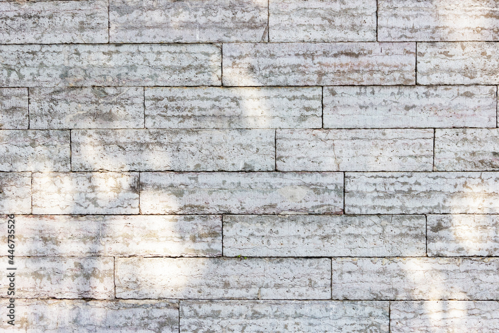 The texture of a gray stone wall made of rectangular marble blocks. Sunlight on the masonry.