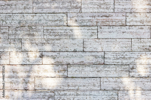 The texture of a gray stone wall made of rectangular marble blocks. Sunlight on the masonry.