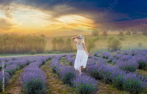 Beautiful young woman in wicker hat and white dress in a lavender field with