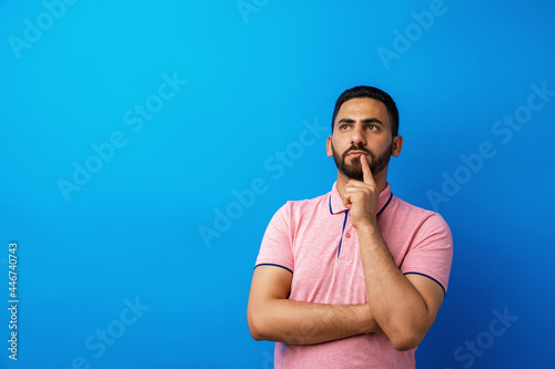 Fotografía Pensive young arab man thinking and looking up against blue background