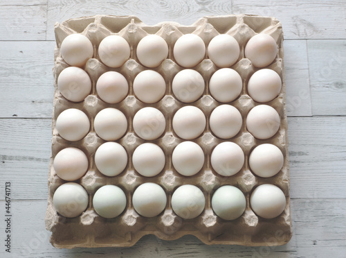 Many duck eggs in carton box on white wood background top view