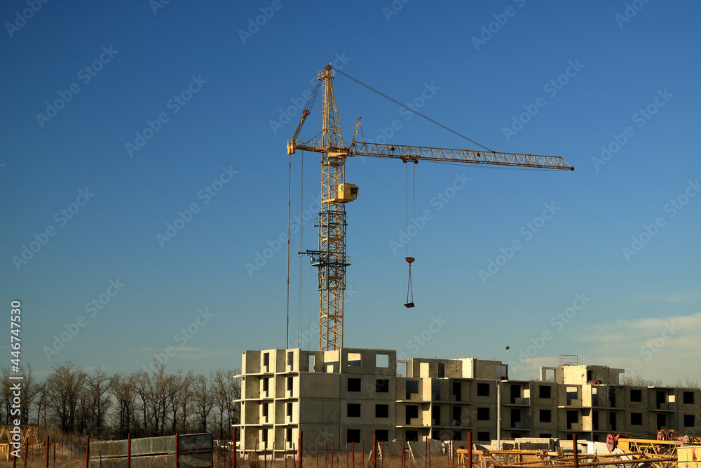 An image of a tower crane against the background of a house under construction. An image of a tower crane against the background of a house under construction.