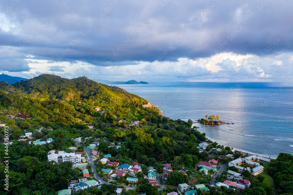 Mahe Island with Port Glaud village drone landscape, with lush tropical forest of Morne Seychellois National Park and Indian Ocean on the horizon, sunset, golden hour.