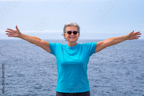 Smiling senior woman standing at the beach with open arms, horizon over water © luciano