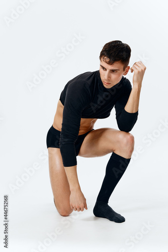 a sporty man in black shorts and a short sweater on a light background stands on his knee in full growth