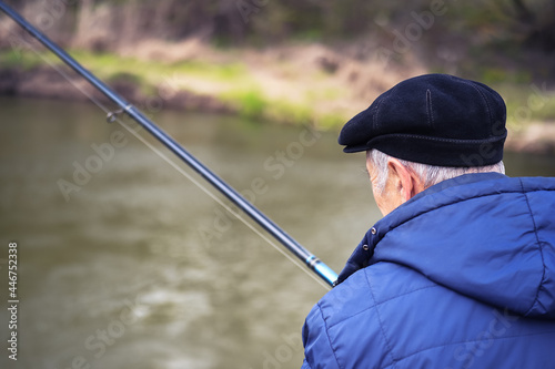 A retired man in close-up fishing in demi-season clothes. Rear view. Background