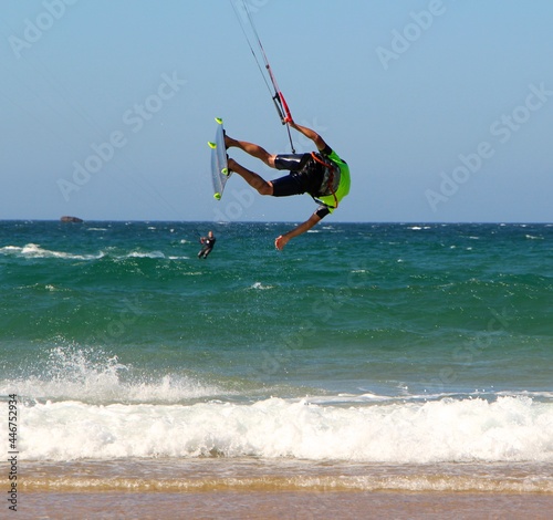 Jumping kitesurfer or kiteboarder hanging sideways Kitesurfing from the beach of Somo on a sunny windy afternoon Santander Cantabria Spain Summer 2020