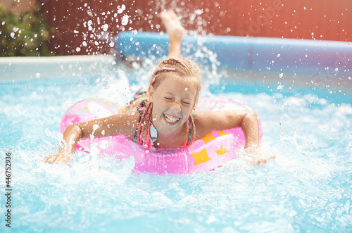 Funny little girl swims in a pool in an pink life preserver
