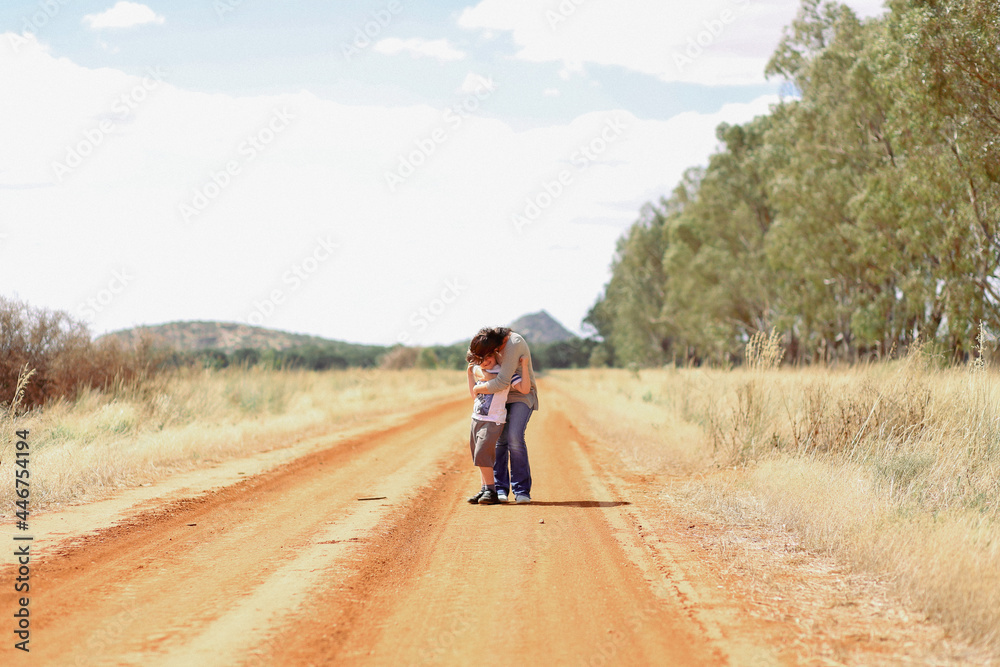 Mother and son standing together in hug on country dirt road