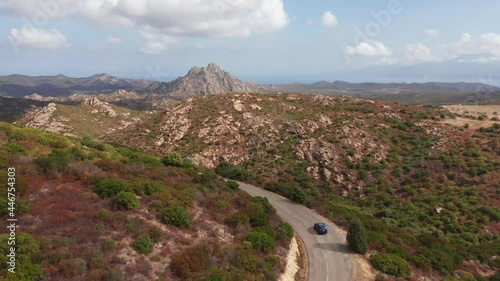 Aerial shot of electric car driving on the sunny desert clean road highway to mountains landscape.Luxury modern vehicle riding fast along trees and fields country road with renewable energy photo