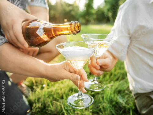 Closeup hand of man pouring champagne in glasses of friends or family outdoor at summer. Celebraiting group of people photo