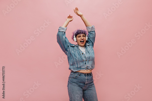 Adult girl in denim jacket and jeans listens to music and sings song on isolated background. Short-haired woman in fashionable outfit dancing..