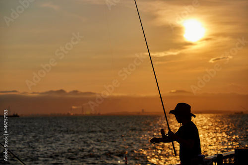 夏の海の海岸で釣りをしている人と鮮やかな夕焼けの風景