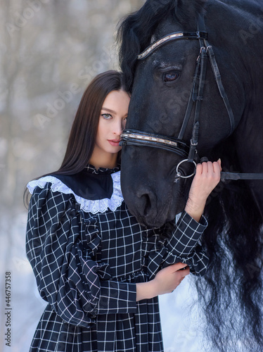 woman with long brown hair and friesian horse close up portrait on winter snowy background