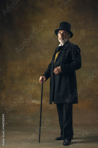 Portrait of elderly gray-haired man, gentleman, aristocrat or actor posing isolated on dark vintage background. Retro style, comparison of eras concept. photo