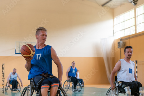 Disabled War veterans mixed race opposing basketball teams in wheelchairs photographed in action while playing an important match in a modern hall. 