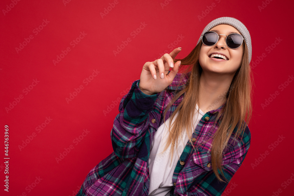 Shot of charming smiling adult blonde woman isolated over red background wearing purple casual shirt and stylish sunglasses looking at camera and having fun Shot of charming smiling adult blonde woman isolated over red background wearing purple casual shirt and stylish sunglasses looking at camera and having fun