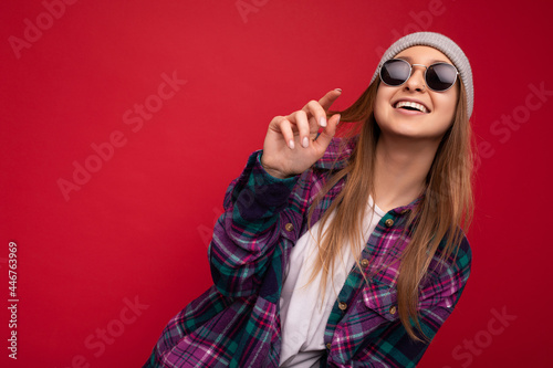 Shot of charming smiling adult blonde woman isolated over red background wearing purple casual shirt and stylish sunglasses looking at camera and having fun
