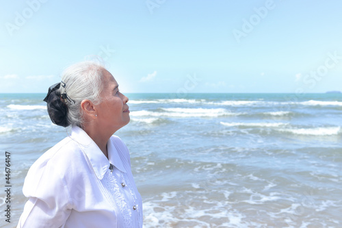 Portrait of elderly old senior woman standing on tropical sea beach outdoor, have fun and enjoy spending time on sand beach, resting and relaxing on holiday vacation. © Stella