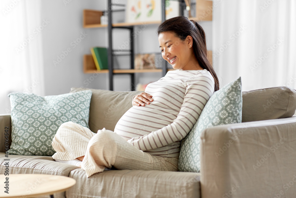 pregnancy, rest, people and expectation concept - happy smiling pregnant asian woman sitting on sofa at home pregnancy, rest, people and expectation concept - happy smiling pregnant asian woman sitting on sofa at home