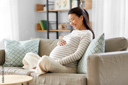 pregnancy, rest, people and expectation concept - happy smiling pregnant asian woman sitting on sofa at home