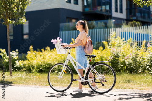people, leisure and lifestyle - happy young woman with flowers in basket of bicycle and backpack walking on city street #446766994
