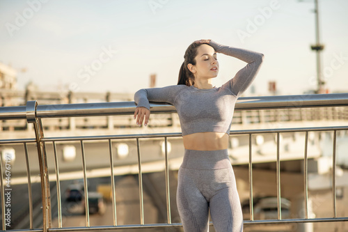 Fit girl in grey sportswear standing at the bridge and looking relaxed