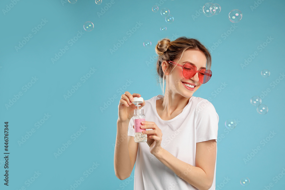 Young woman blowing soap bubbles on light blue background, space for text Young woman blowing soap bubbles on light blue background, space for text