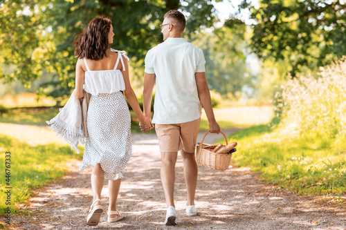 leisure  vacation and people concept - happy couple with picnic basket and blanket walking at summer park