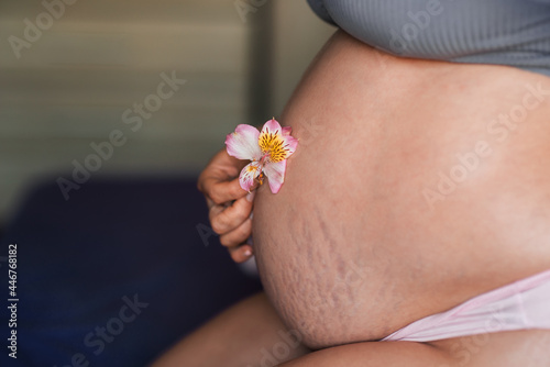 Pregnant woman's stomach is close-up with a gentle beautiful flower. Natural skin texture of pregnant woman
