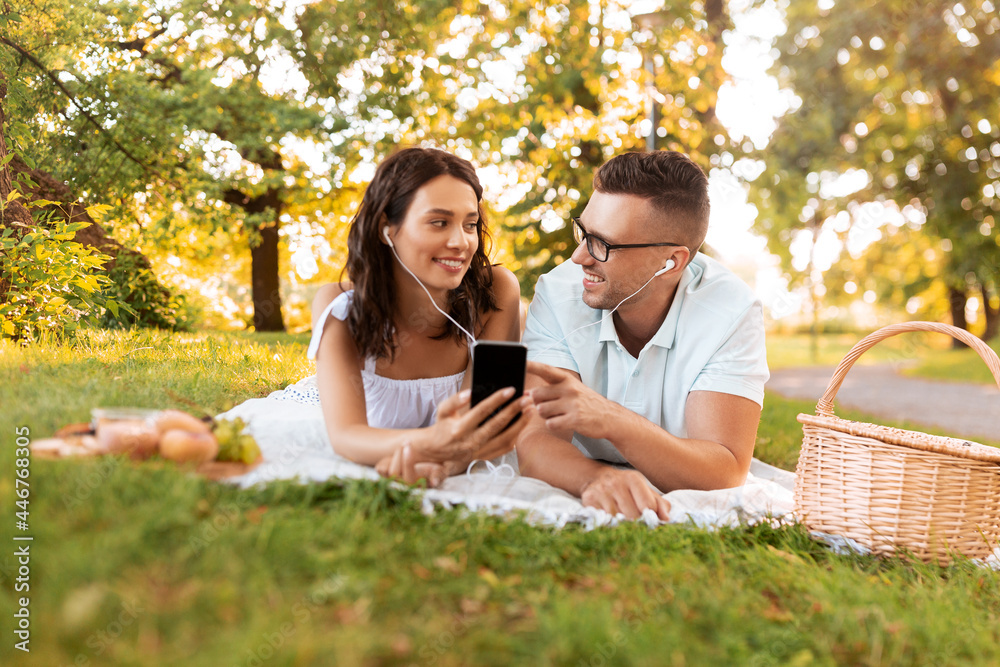 leisure, vacation and people concept - happy couple with earphones and smartphone listening to music on picnic blanket at summer park leisure, vacation and people concept - happy couple with earphones and smartphone listening to music on picnic blanket at summer park