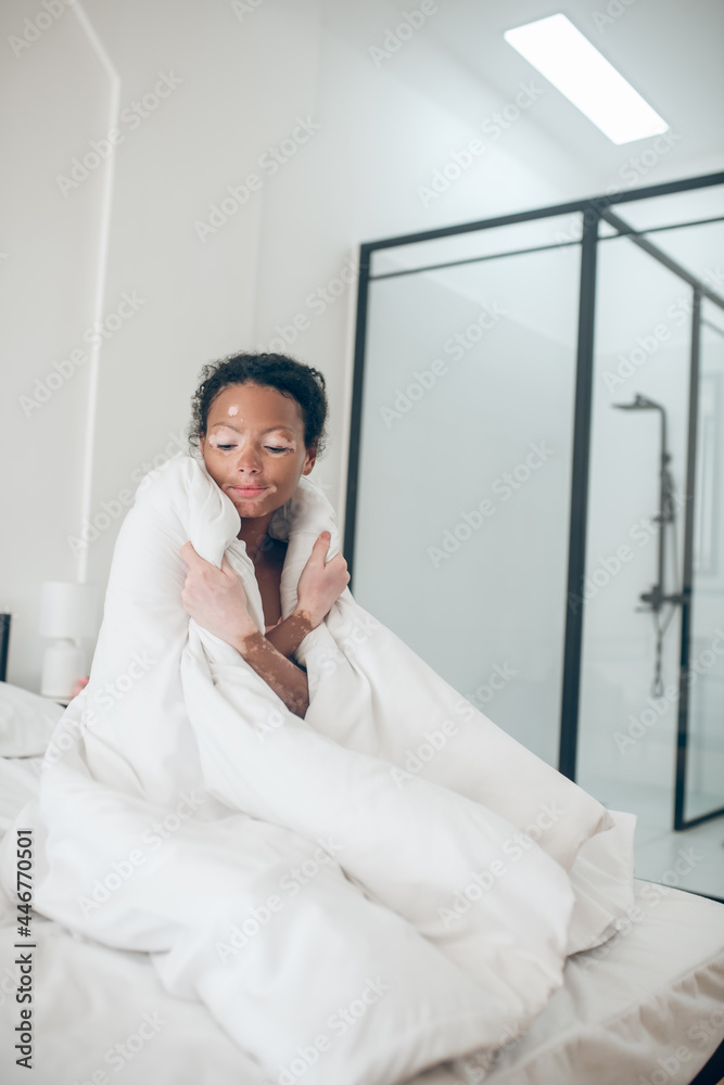 Young woman sitting in bed covered with blanket and feeling relaxed Young woman sitting in bed covered with blanket and feeling relaxed