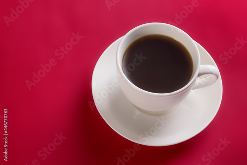 White cup with hot aromatic coffee on a saucer on a red background