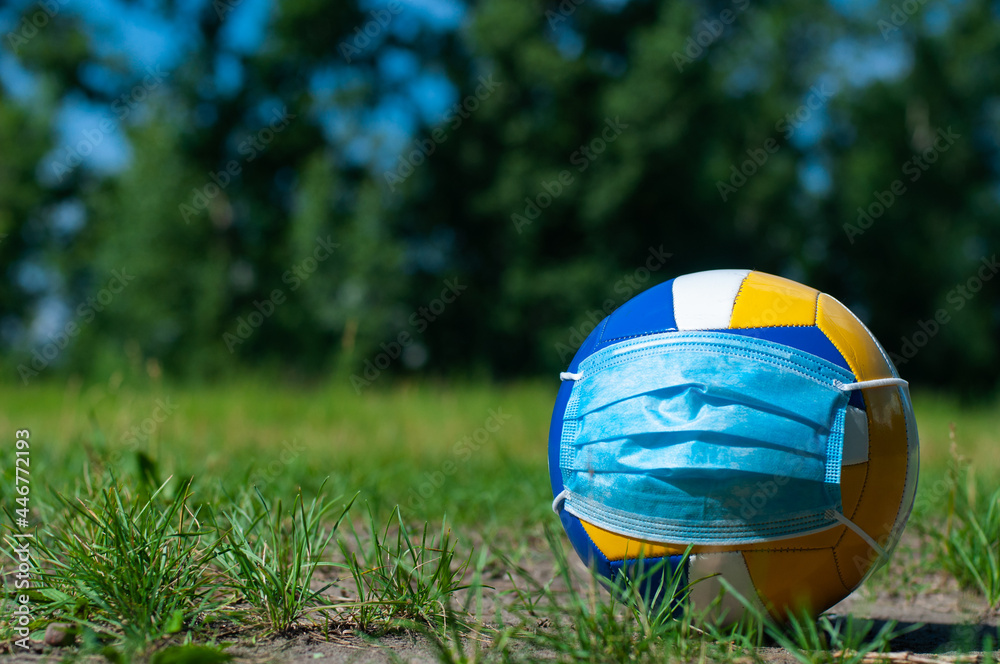 A volleyball with a face mask on the grass. Copy space.