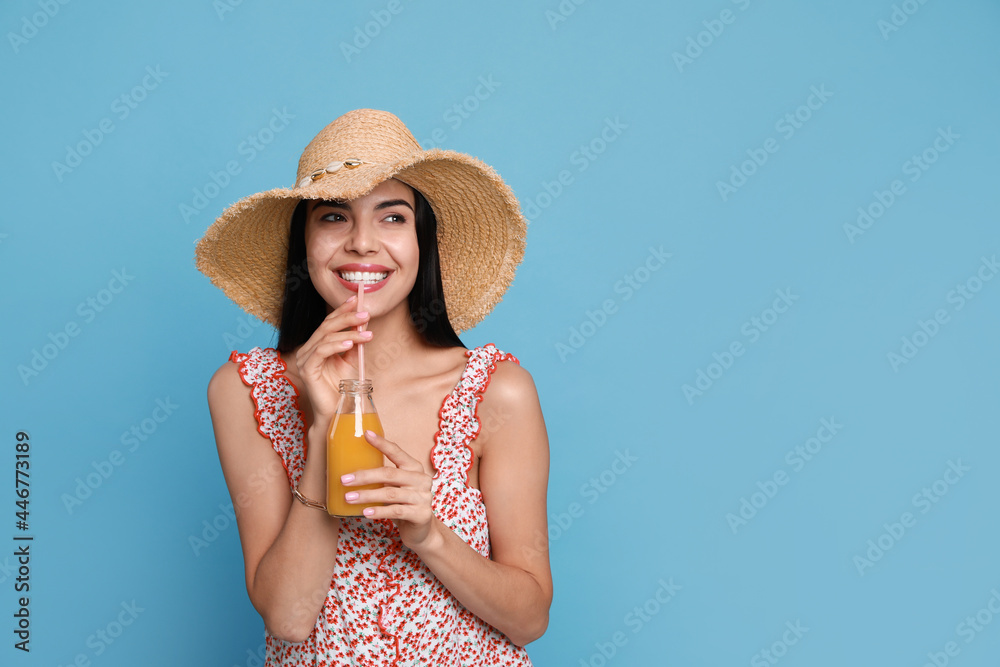 Beautiful young woman with straw hat and bottle of refreshing drink on light blue background. Space for text