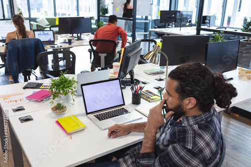 Mixed race male creative worker sitting at desk using laptop