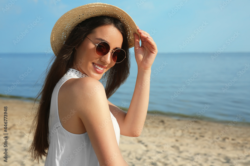Beautiful young woman with straw hat and sunglasses on beach. Stylish headdress