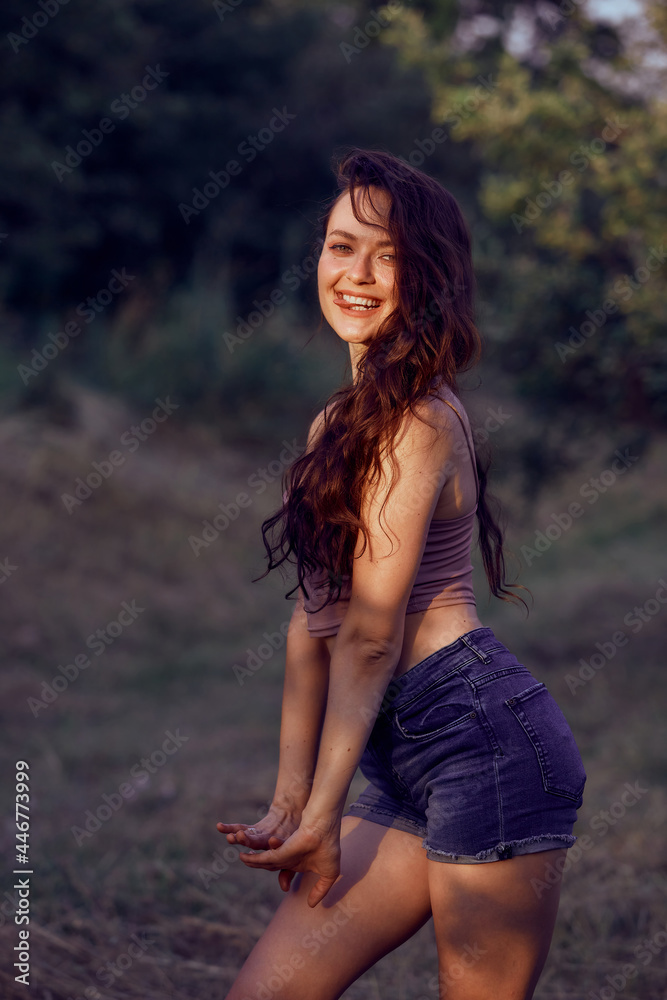 Beautiful woman enjoying the summer sun outdoors in the park. Dressed jeans shorts and beige top in golden hour Beautiful woman enjoying the summer sun outdoors in the park. Dressed jeans shorts and beige top in golden hour