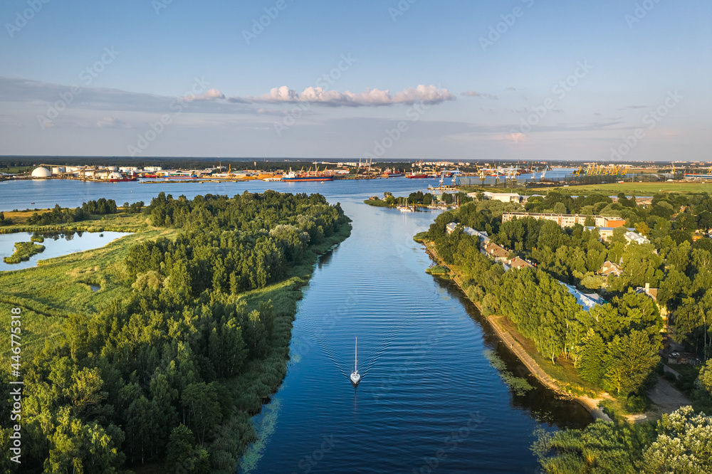 Riga port loading terminal with container ships. Boats and yachts riding on river. Industrial territory meets sustainable environment.
