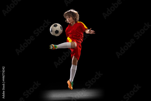 Fototapeta Naklejka Na Ścianę i Meble -  One little male football soccer player, boy training with football ball isolated on dark studio background. Concept of sport, game, hobby