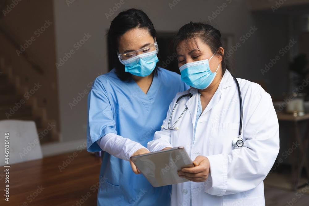 Two asian female doctors wearing face masks at home using tablet Two asian female doctors wearing face masks at home using tablet