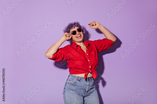 Sunny bright girl in red long-sleeved shirt tied at waist. Short-haired woman with lilac hair in jeans and glasses smiling.. © Look!