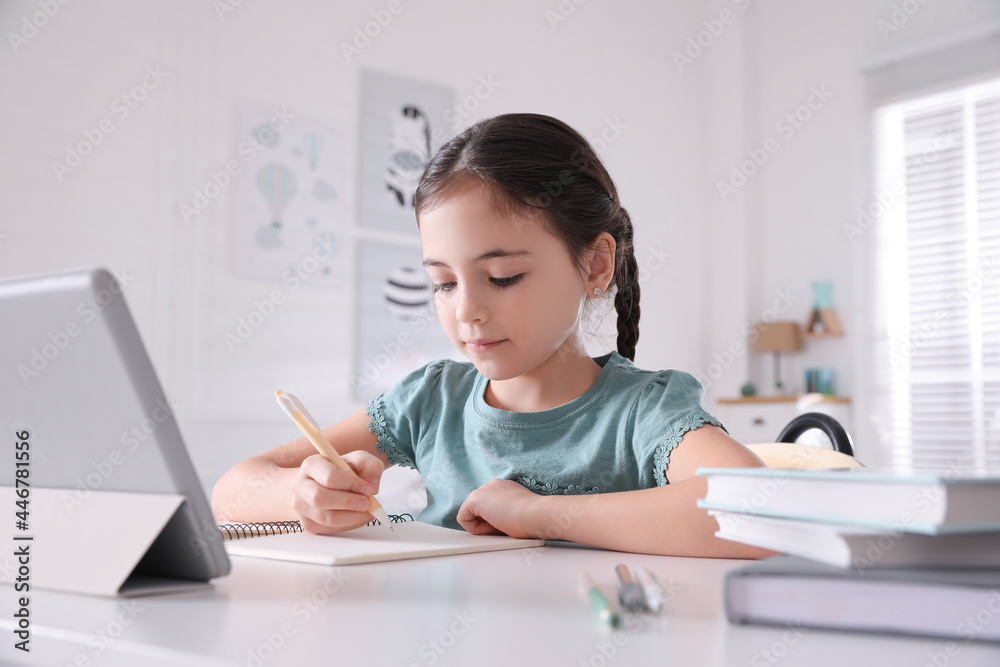 Little girl doing homework with tablet at table in room Little girl doing homework with tablet at table in room