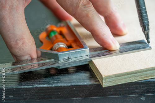 selected focus of a caprpenter marking out a meaurement on  a piece of birch plywood using an adjustable calibrated square and a mechanical pencil
