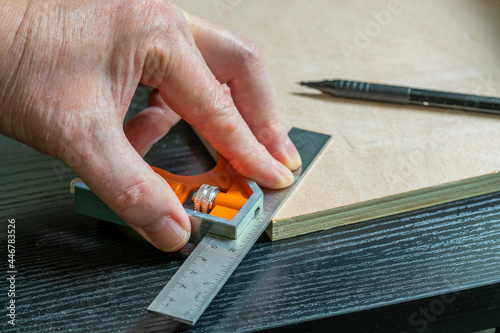 selected focus of a caprpenter marking out a perfect forty five degree angle on a piece of plywood using an adjustable calibrated square and a mechanical pencil