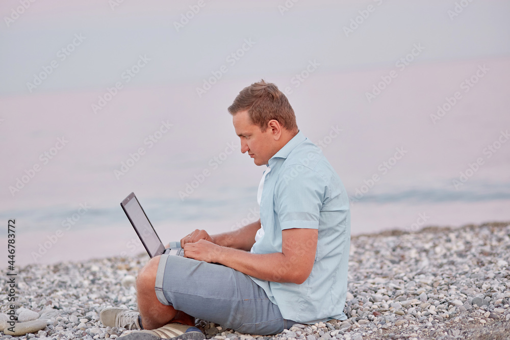 Man brunette with a laptop on a on the beach. Freelancer, working remotely, webinar, learning concept, chatting with friends. New normal concept.