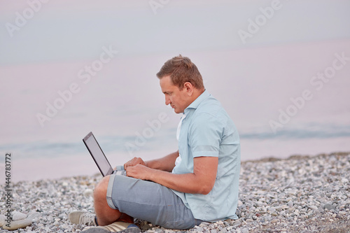 Man brunette with a laptop on a on the beach. Freelancer, working remotely, webinar, learning concept, chatting with friends. New normal concept.